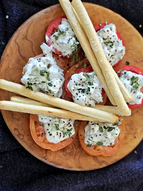 Overhead shot of plateful of tomatoes topped with easy yogurt cucumber dip and breadsticks.