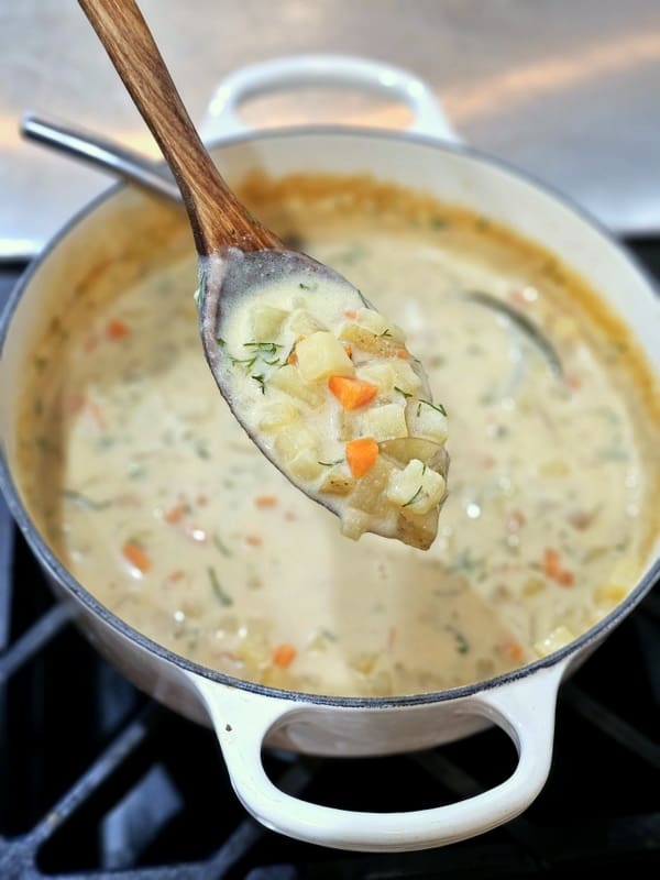 Closeup shot of spoonful of rustic Croatian style potato soup over pot of more soup